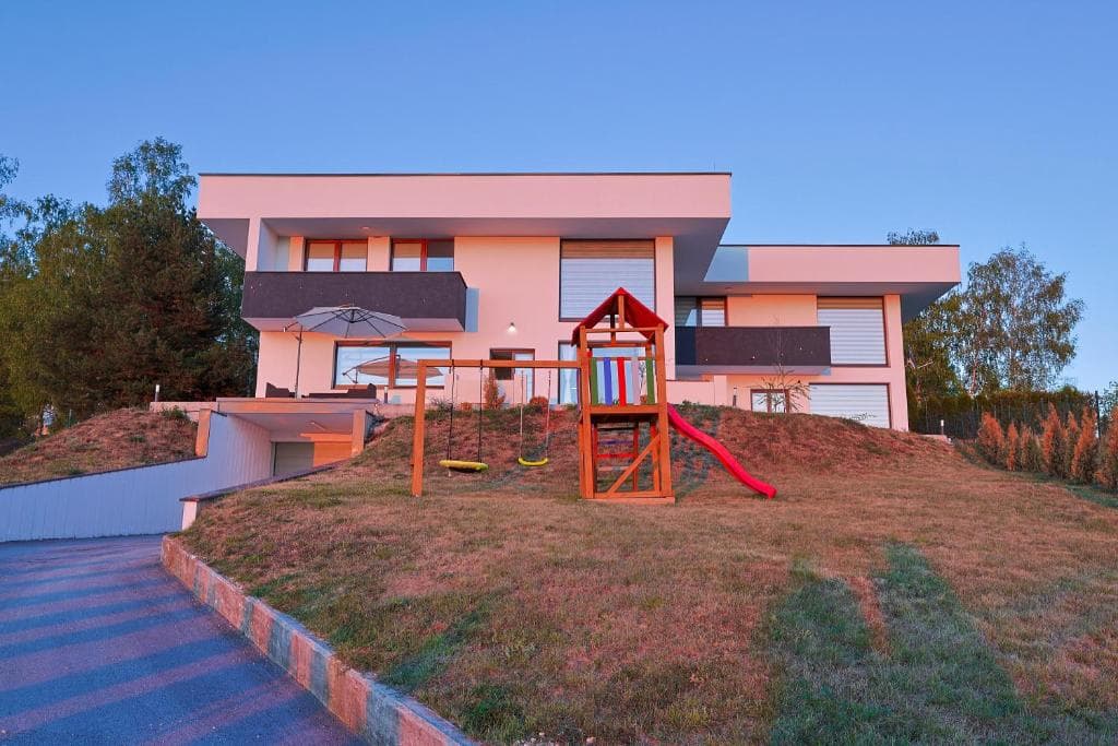 Full exterior of Villa 1 with modern balconies, a garden and a children’s play area