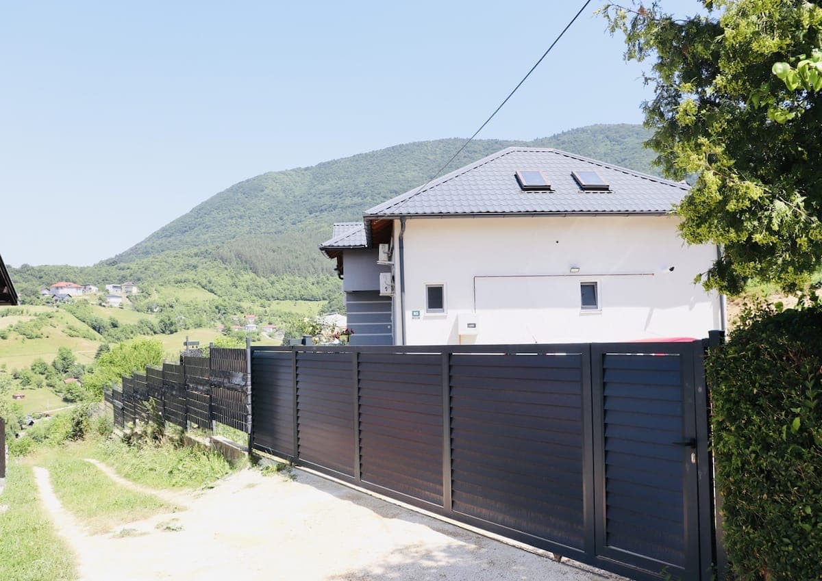 Exterior of Villa 2 with a grey roof, garden fence and green mountain backdrop